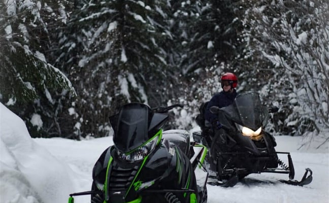 Two snowmobiles on a groomed trail through snow-covered pines in Northern Wisconsin
